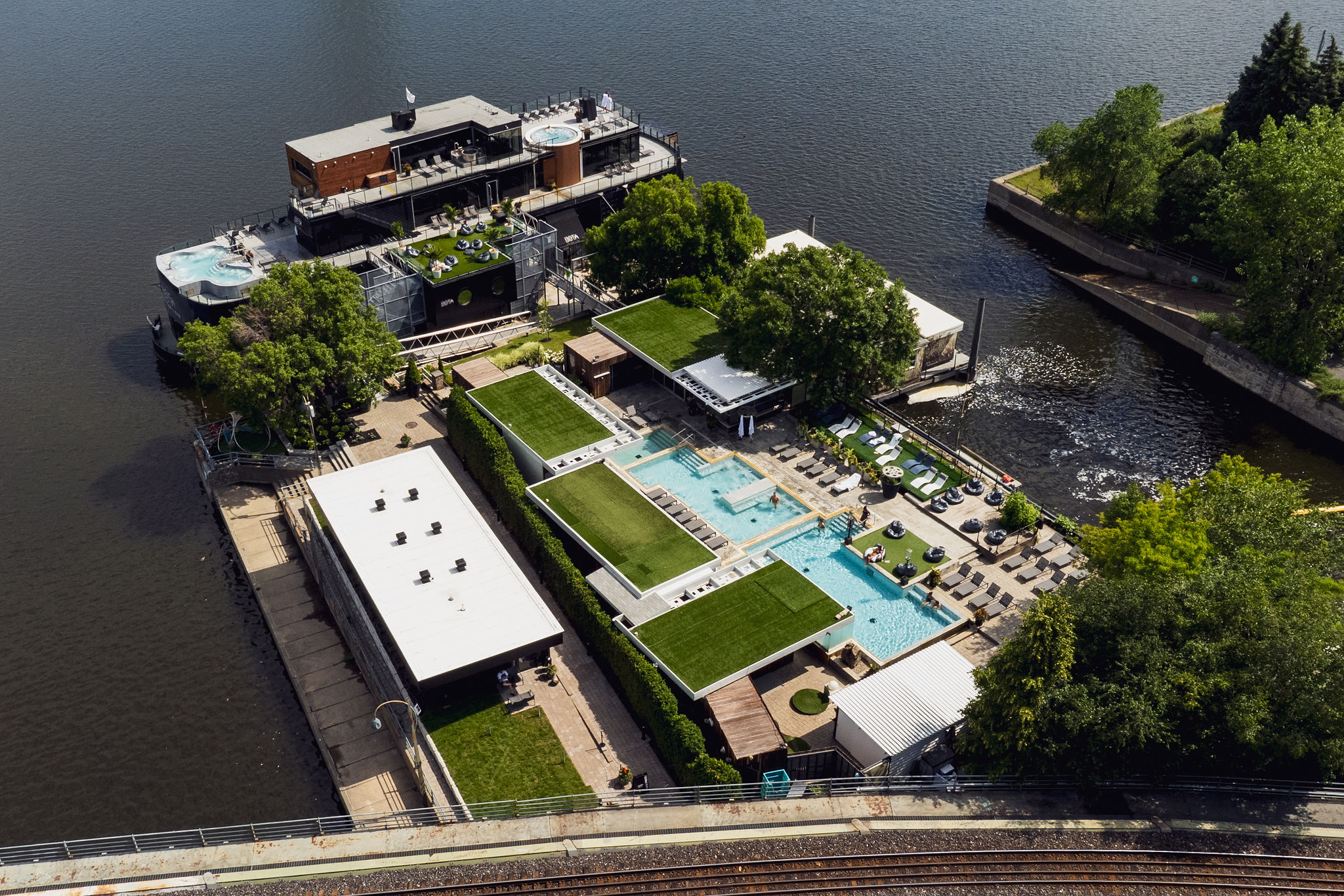 Vue aérienne du spa Bota Bota, situé sur une péniche dans le Vieux-Port de Montréal, montrant les bassins extérieurs, les terrasses verdoyantes et les installations sur l’eau, en été.