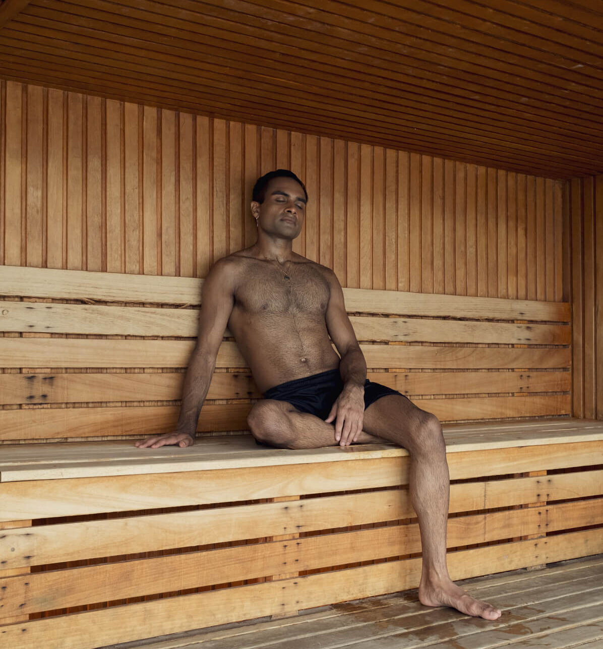 Homme assis et détendu dans un sauna en bois, les yeux fermés, profitant de la chaleur. /Man sitting relaxed in a wooden sauna, eyes closed, enjoying the heat.