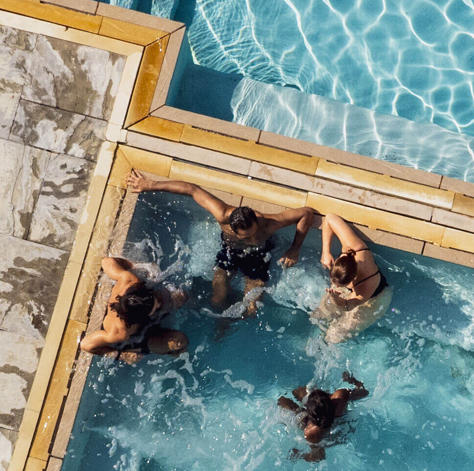 Groupe d’amis profitant d’un bain extérieur chauffé, assis dans l’eau près du rebord. / Group of friends enjoying an outdoor heated bath, sitting in the water near the edge.